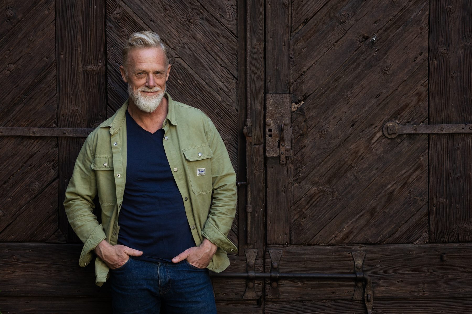 Torbjörn Hellmouth i grön skjortjacka, lutad mot en gammal träport med järnbeslag.