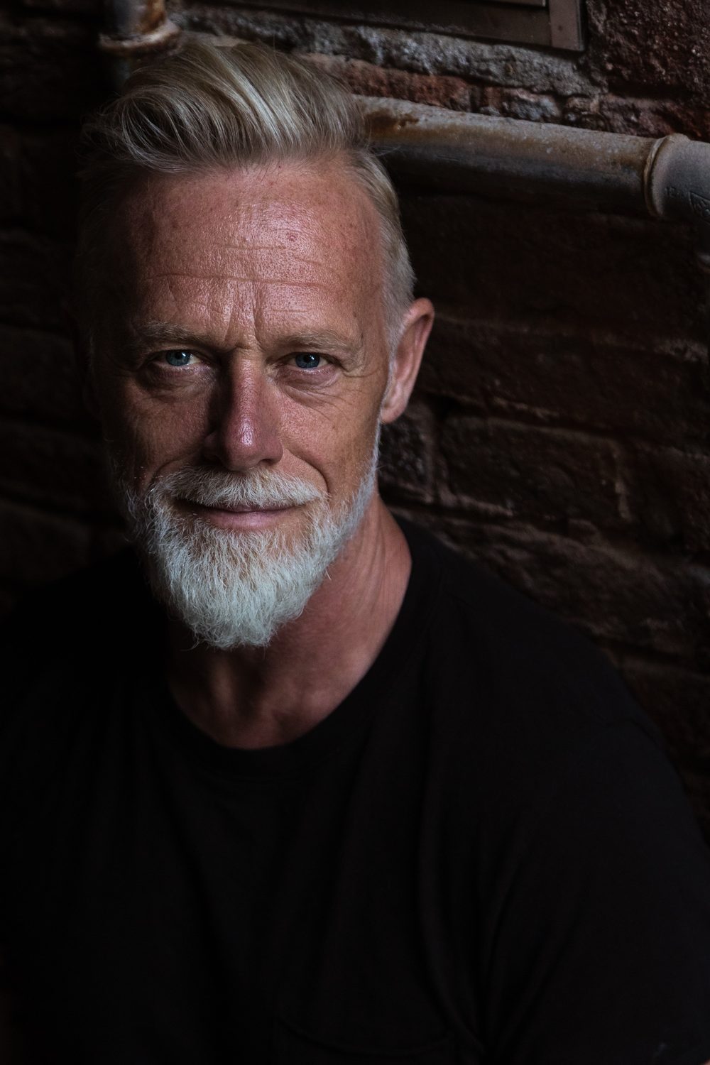 Torbjörn Hellmouth i svart tröja, allvarlig blick, i dämpat ljus mot en mörk stenvägg.